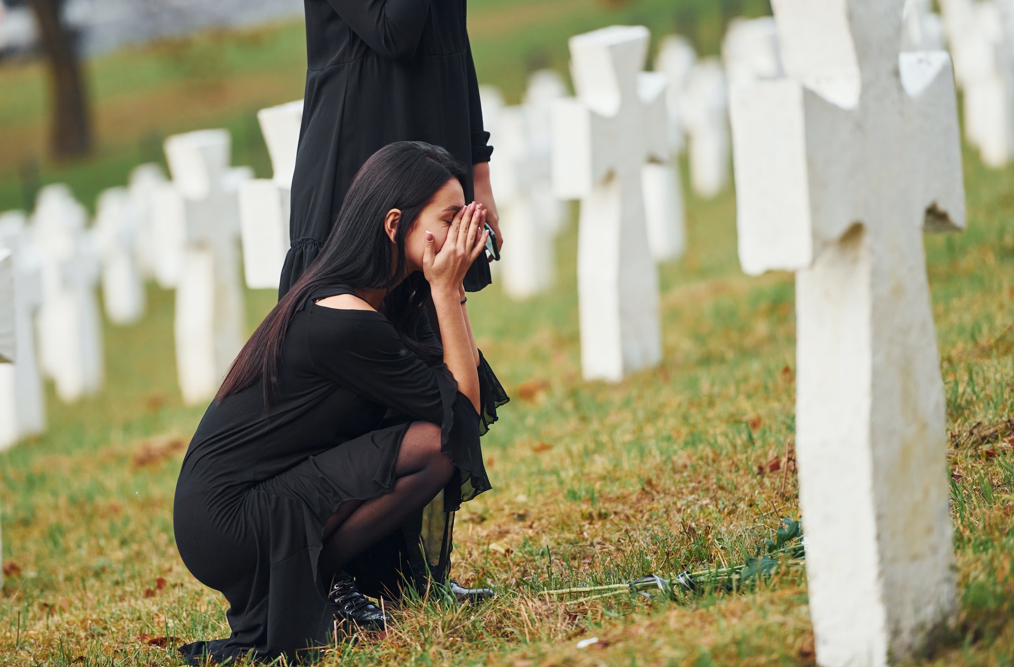 Two young women in black clothes visiting cemetery with many white crosses